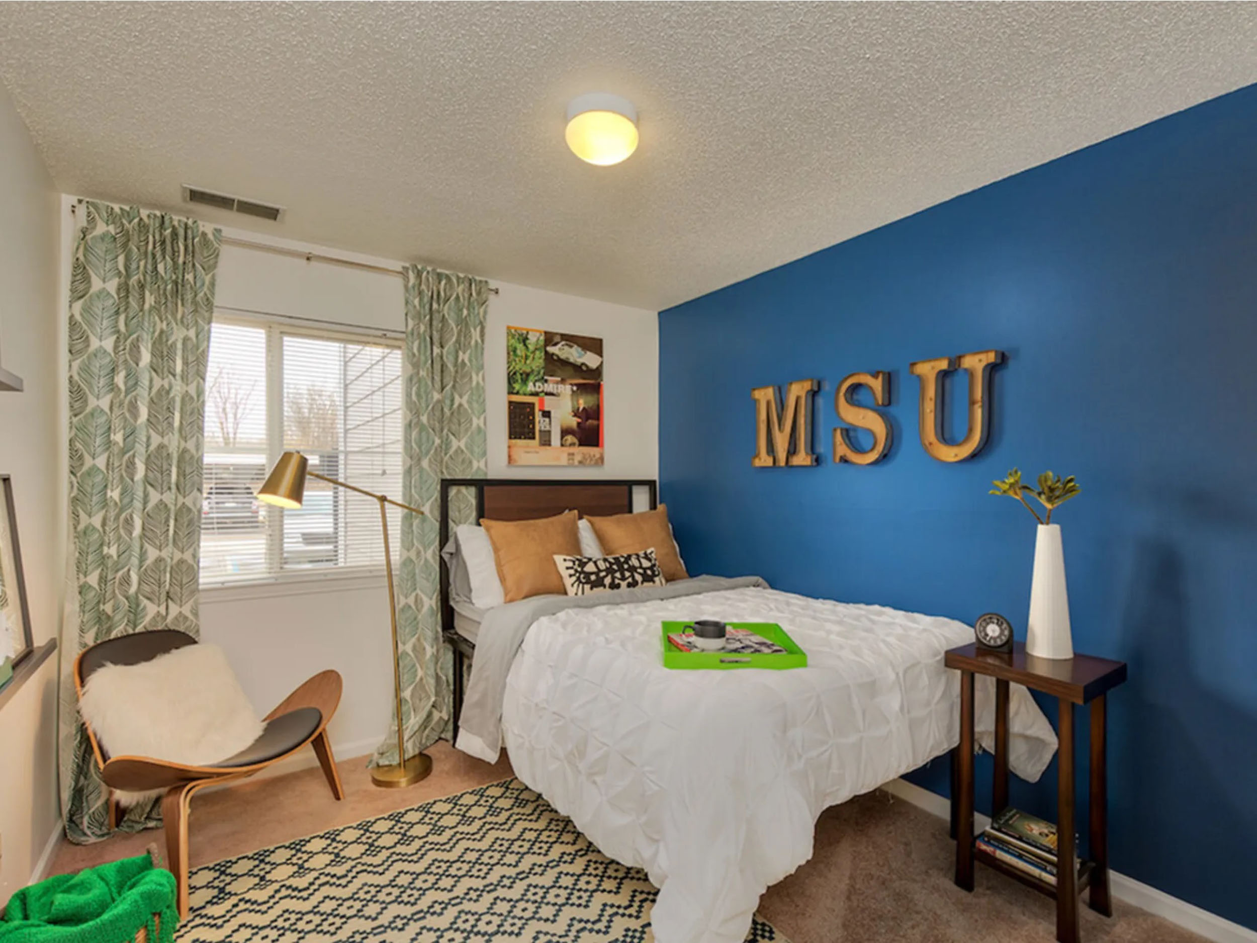 Bedroom with blue accent wall MSU sign and bed